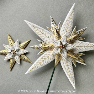May include: Two white and gold star-shaped ornaments with beaded accents. The larger star has a green stem.