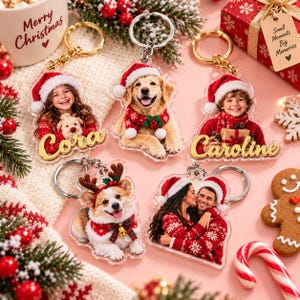 Pode incluir: Cinco porta-chaves em acrílico personalizados com fotos temáticas de Natal de pessoas e animais de estimação com gorros de Pai Natal e camisolas festivas. Dois porta-chaves incluem os nomes Cora e Caroline em letra cursiva dourada.