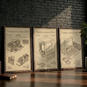 May include: Three framed patent prints of early computer technology. The prints include a computer, monitor, and laptop, each with detailed diagrams and text. The frames are brown, and the background is a dark brick wall.