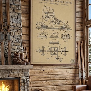 May include: A framed patent print of a releasable ski binding device from 1975, displayed in a rustic cabin setting. The print features detailed technical drawings of the ski binding. The room includes a fireplace, skis, and leather boots.