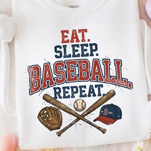 May include: White sweatshirt with the text "EAT. SLEEP. BASEBALL. REPEAT." in red and blue. The design includes crossed baseball bats, a baseball, a glove, and a baseball cap.
