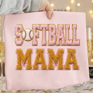 May include: A pink cushion featuring the embroidered text "SOFTBALL MAMA". The word "SOFTBALL" is in pink with gold edging, and a baseball is in the center. "MAMA" is in gold, creating a sporty design.