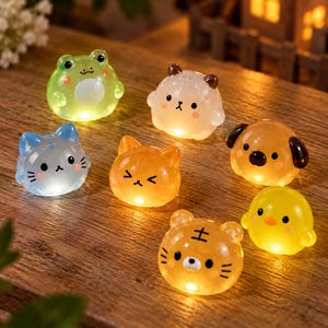 May include: A collection of seven small, translucent, glowing animal-shaped figurines including a green frog, a white bear, a blue cat, an orange cat, a brown dog, a yellow chick, and an orange tiger, all featuring simple facial expressions.