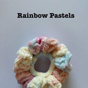 May include: A pastel rainbow colored scrunchie made of fluffy yarn. The scrunchie is in the shape of a donut.