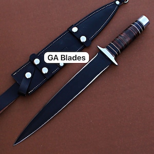 Può includere: Un pugnale nero con una lama lucida e un manico marrone e argento, accompagnato da un fodero in pelle nera. Il testo "GA Blades" è visibile. Il pugnale ha una lama a doppio taglio e una guardia.
