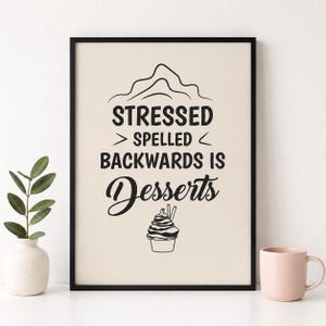 May include: A framed wall art print featuring a cream-coloured background with black text that reads STRESSED SPELLED BACKWARDS IS Desserts. Above the text is a simple line drawing of a mountain, and below is a graphic of a soft serve ice cream cone.