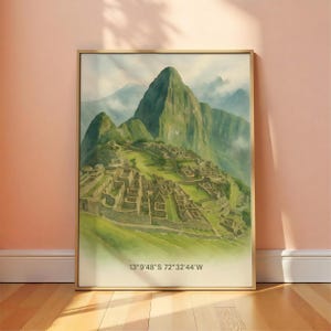 May include: Watercolor painting of Machu Picchu, Peru, framed in gold. The artwork depicts the ancient Inca citadel nestled in a green mountain landscape with a cloudy sky. Coordinates 13°9'48"S 72°32'44"W are printed at the bottom.