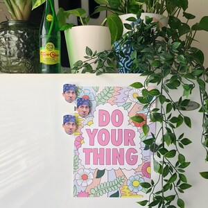 Pode incluir: Um refrigerador branco com um p&ocirc;ster que diz "Do Your Thing" em letras rosa. O p&ocirc;ster tem um design floral e tr&ecirc;s &iacute;m&atilde;s com o rosto de um homem.
