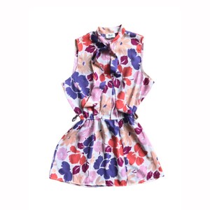 Puede incluir: Un vestido sin mangas de estampado floral con cuello de lazo y cintura fruncida. El vestido es en tonos de rosa, naranja, morado y blanco.