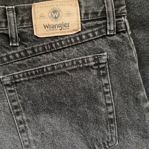 May include: A close-up of a black pair of Wrangler jeans with a back pocket and a label that reads "Premium Quality" and "Wrangler Authentic Jeans".