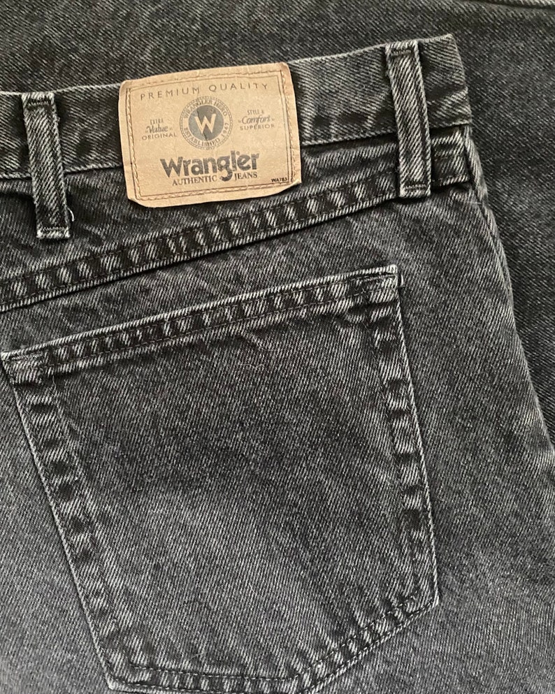 May include: A close-up of a black pair of Wrangler jeans with a back pocket and a label that reads "Premium Quality" and "Wrangler Authentic Jeans".