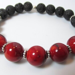 May include: A bracelet made with black lava stone and red coral beads. The beads are separated by silver-coloured metal spacers. The bracelet is strung on elastic. A simple, elegant piece of jewellery.