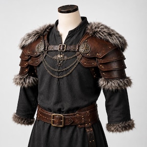 May include: A dark brown leather shoulder armor set with layered plates, brass-toned studs, and faux fur trim. The piece features a chest strap with a buckle, decorative circular emblems, and three draped metal chains across the front chest area.