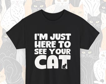 May include: Black t-shirt with white text that reads "I'm just here to see your cat". The text is in a bold, playful font. A small silhouette of a cat is at the bottom of the text.