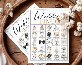 May include: Two wedding bingo cards with illustrations of wedding-related items like a cake, rings, and a dress. The cards are on a wooden tray with white flowers and the text "Wedding BINGO".