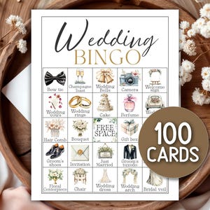 May include: A wedding bingo game card with various wedding-themed illustrations, including a bow tie, wedding rings, and a wedding cake. The card reads "Wedding BINGO" and includes a circular label that says "100 CARDS". The card is set on a wooden tray.