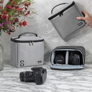 May include: Grey camera bag with a black zip and handle, with the brand name "boono" visible. The bag is shown with a Canon camera and lens. A second grey bag is also shown, with the word "Salt" printed on it.