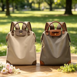 May include: Two backpacks with top handles and shoulder straps. The left backpack is beige with a brown flap featuring the name Ruby. The right backpack is gray with a brown flap featuring the name Carter. Both have gold-tone hardware and brown trim.