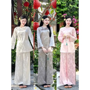 Könnte beinhalten: Drei Frauen in passenden Seiden-Outfits in Creme, Taupe und Rosa. Jedes Ensemble besteht aus einem langärmeligen Oberteil und einer Hose mit weitem Bein und dezentem Blumenmuster. Die Oberteile haben einen runden Ausschnitt und die Hosen sind bodenlang.