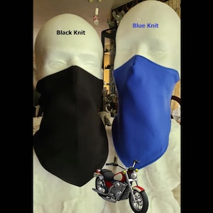May include: Two neck gaiters, one black and one blue, are displayed on mannequins. The mannequins are wearing white shirts. The text "Black Knit" is above the black neck gaiter and the text "Blue Knit" is above the blue neck gaiter. A red motorcycle is in the foreground.