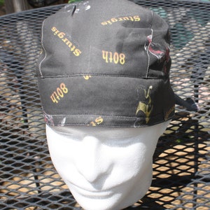 May include: Black and yellow patterned bandana with the text "Sturgis" and "408" repeated on the fabric. The bandana is worn on a white mannequin head.