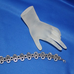 May include: A silver bracelet made of linked metal nuts. The bracelet is on a blue surface.