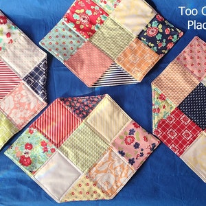 May include: Four colorful quilted placemats with a patchwork design. Each mat is made of different fabrics with various patterns and colors, including red, blue, green, yellow, and white. The placemats are arranged on a blue surface. The text "Too Charming Place Mats" is displayed above the placemats.