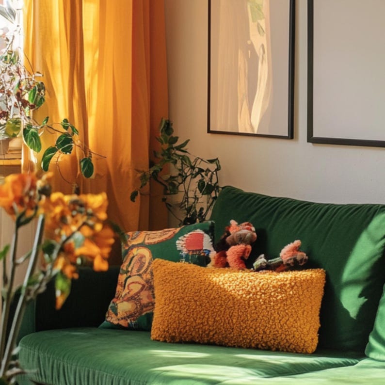 K&ouml;nnte beinhalten: Ein gr&uuml;nes Samtsofa mit einem gelben Kissen und einem gemusterten Kissen. Das Sofa steht vor einem Fenster mit gelben Vorh&auml;ngen und zwei gerahmten Bildern an der Wand.