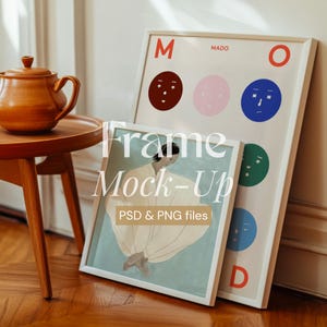 May include: Two white picture frames with different images inside. The frame on the left has a painting of a person wearing a white dress. The frame on the right has a colorful design with the word "MADO" and the letters "M" and "O" at the top and bottom of the frame.
