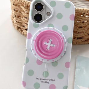 Op de afbeelding: Een witte smartphonehoes met een patroon van lichtgroene en roze stippen. In het midden is een ronde, roze knopvormige grip bevestigd. De tekst "The Wonderful Girl Nice Day" staat in het zwart gedrukt bij de onderkant van de hoes.