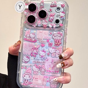 Puede incluir: Funda transparente para teléfono con diseños rosas y blancos de Hello Kitty y My Melody. La funda presenta múltiples ilustraciones y texto en coreano y japonés. La funda está sujeta por una persona.