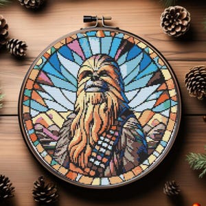 May include: A circular embroidery hoop containing a cross-stitch pattern of a Wookiee character. The design features a stained-glass style background with blue, orange, and white geometric segments surrounding the central brown fur figure.