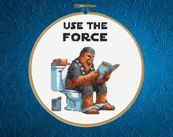 May include: A white cross-stitch embroidery hoop with a brown Wookiee character sitting on a toilet and reading a book. The text "USE THE FORCE" is above the character.