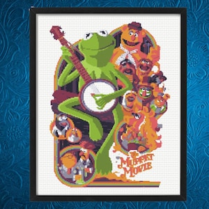 以下が含まれることがあります： フレームに入ったクロスステッチアート。カーミットがバンジョーを演奏し、他のマペットのキャラクターに囲まれています。アートワークはレトロなスタイルで、鮮やかな緑、オレンジ、紫の色合いを使用しています。「The Muppet Movie」の文字が見えます。