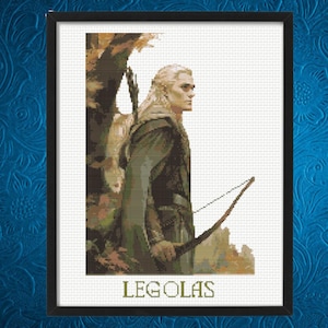 May include: Framed cross-stitch artwork depicting Legolas from The Lord of the Rings. The image shows Legolas in profile, holding a bow, set against a forest background. The name "LEGOLAS" is printed in green at the bottom.