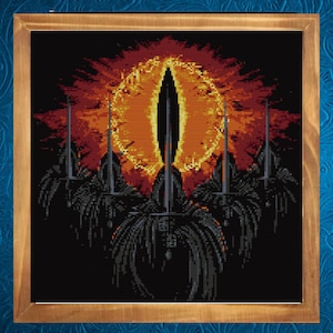 Può includere: Opera d'arte a punto croce incorniciata in una cornice di legno. Il design presenta un occhio centrale nei toni dell'arancione e del giallo, circondato da un'esplosione di fuoco. Sotto l'occhio, figure scure e stilizzate con elementi a forma di spada, su sfondo nero.