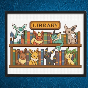 Peut inclure: Broderie au point de croix représentant des créatures de dessins animés dans une bibliothèque. Le mot "LIBRARY" est affiché au-dessus de l'étagère. Les créatures sont de couleurs variées, et les livres sont de différentes couleurs.