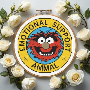 May include: A cross-stitch hoop featuring a cartoon character with the text "EMOTIONAL SUPPORT ANIMAL" in a yellow and blue design. The hoop is surrounded by white roses and green leaves.