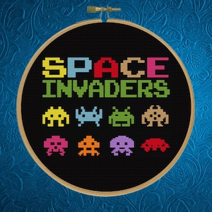 May include: A black embroidery hoop with the text "SPACE INVADERS" in colorful letters.  The hoop features a row of pixelated alien spaceships in various colors.