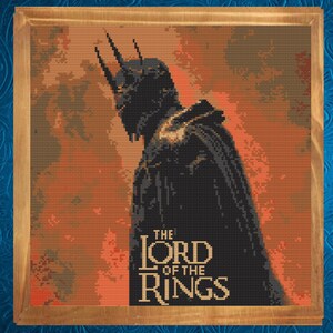 May include: Cross-stitch artwork of a dark figure from "The Lord of the Rings" framed in a wooden border. The figure is silhouetted against an orange and red background. The title "The Lord of the Rings" is displayed in white text.