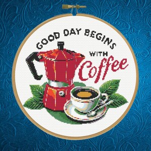 May include: A cross-stitch embroidery in a circular wooden hoop featuring a red moka pot, a white coffee cup on a saucer with a spoon, and green leaves. The text reads, "GOOD DAY BEGINS WITH Coffee" in black and red stitched lettering.