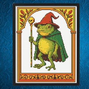 Puede incluir: Un patrón de punto de cruz enmarcado que presenta una rana en pixel art con un sombrero rojo puntiagudo y una capa verde. La rana sostiene un bastón rematado con una calavera. El diseño está encerrado en un borde de arco amarillo y naranja.