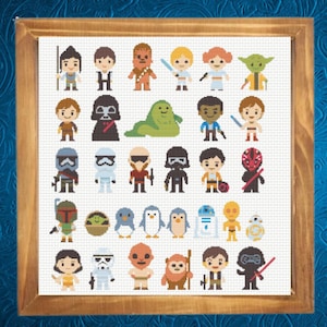 May include: A framed cross-stitch sampler featuring a grid of thirty-two pixelated characters from the Star Wars universe, including various heroes, villains, droids, and creatures, all rendered in colorful thread on a white fabric background.