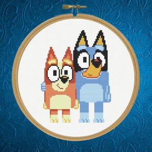 May include: A cross-stitch embroidery piece featuring two cartoon dogs, one orange and one blue, displayed in a round wooden hoop. The design is stitched on white fabric, showcasing the characters standing side-by-side with a simple, pixelated style.