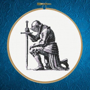 May include: Cross-stitch of a knight kneeling, holding a sword, in shades of grey and white. The design is set within a round frame, mounted on a blue background with a floral pattern. The knight is wearing full armour.