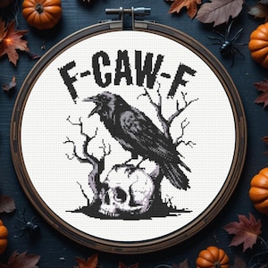 May include: A cross-stitch design in a wooden hoop features a black crow perched on a skull, with bare tree branches and the text "F-CAW-F". The design is surrounded by pumpkins, leaves, and spiders, creating a Halloween theme.