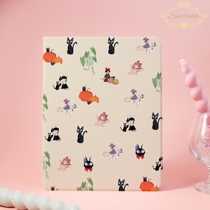 Pode incluir: Uma capa de tablet bege com um padrão repetido de gatos pretos, abóboras e personagens de desenhos animados. O design inclui bruxas em vassouras e meninas em vestidos rosa. O logotipo Suchakk está no canto superior direito.
