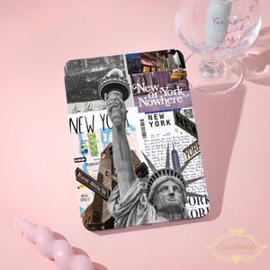 May include: A decorative case with a New York City collage design, featuring the Statue of Liberty, cityscapes, and street signs. The case has the words "New York" and "East 40th St" printed on it. The background is a soft pink.