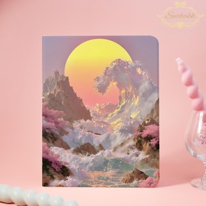 Könnte beinhalten: Ein Notizbuch mit einer lebendigen Illustration einer großen Ozeanwelle, die gegen felsige Klippen unter einer gelben Sonne schlägt. Das Kunstwerk zeigt rosa Kirschblüten und eine weiche, pastellfarbene Farbpalette. Das Suchakk-Logo befindet sich in der oberen rechten Ecke.