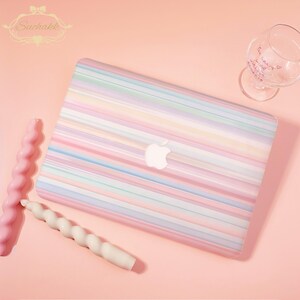 May include: A laptop case featuring a horizontal striped pattern in pastel shades of pink, blue, yellow, and lavender. The case has a central cutout for an Apple logo. Two spiral-shaped taper candles in pink and white are positioned nearby.